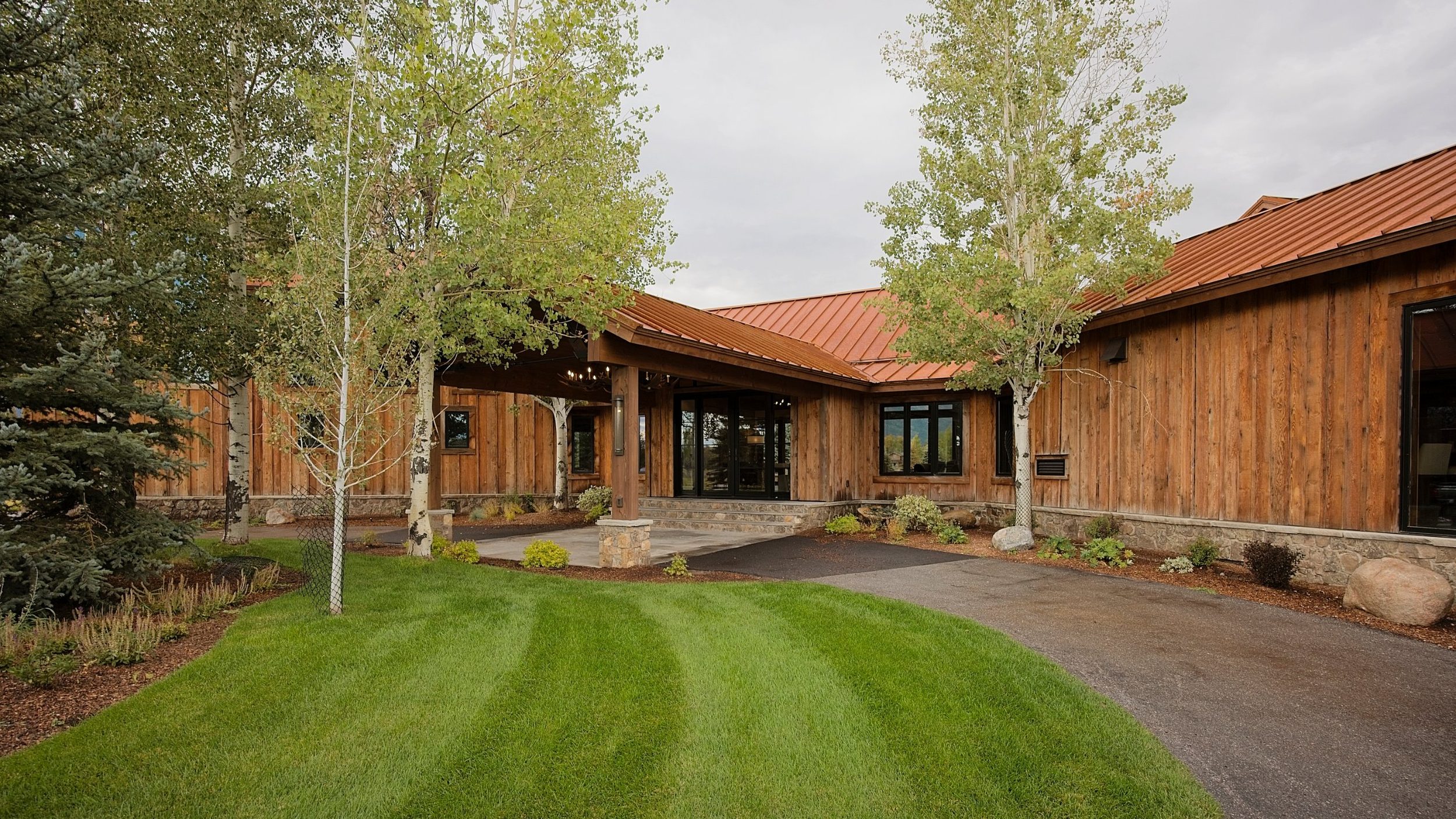 Timber-framed covered entry with stone piers and aspen trees at a custom mountain home