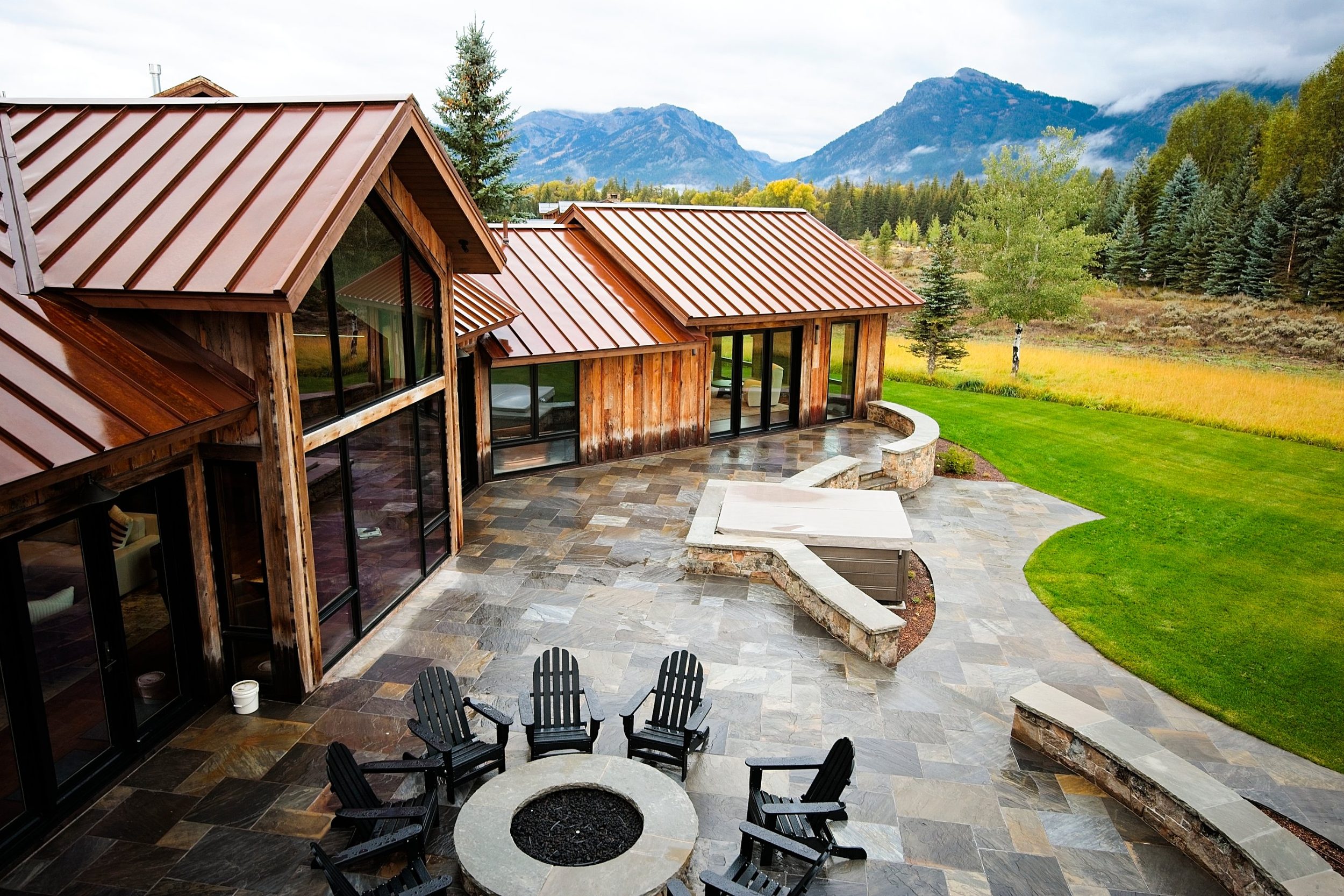 Stone terrace with fire pit, spa, and copper-toned metal roofs facing the mountains