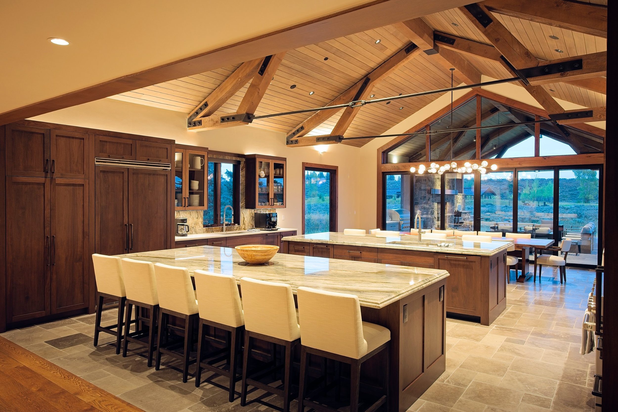 Kitchen with two quartzite islands, walnut cabinetry, and exposed timber trusses opening to the terrace