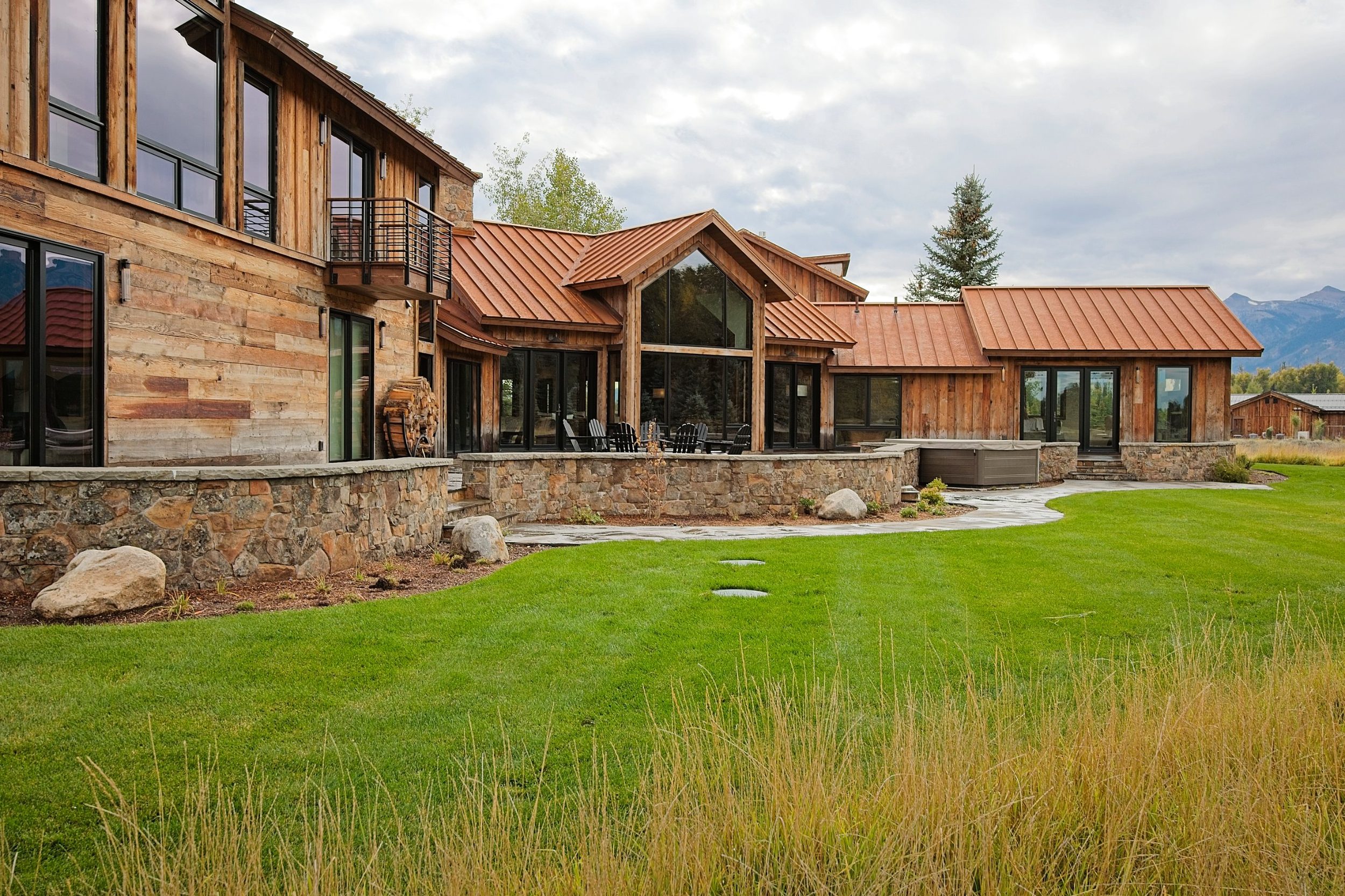 Stone-walled terrace and glass gable of a reclaimed timber mountain ranch home