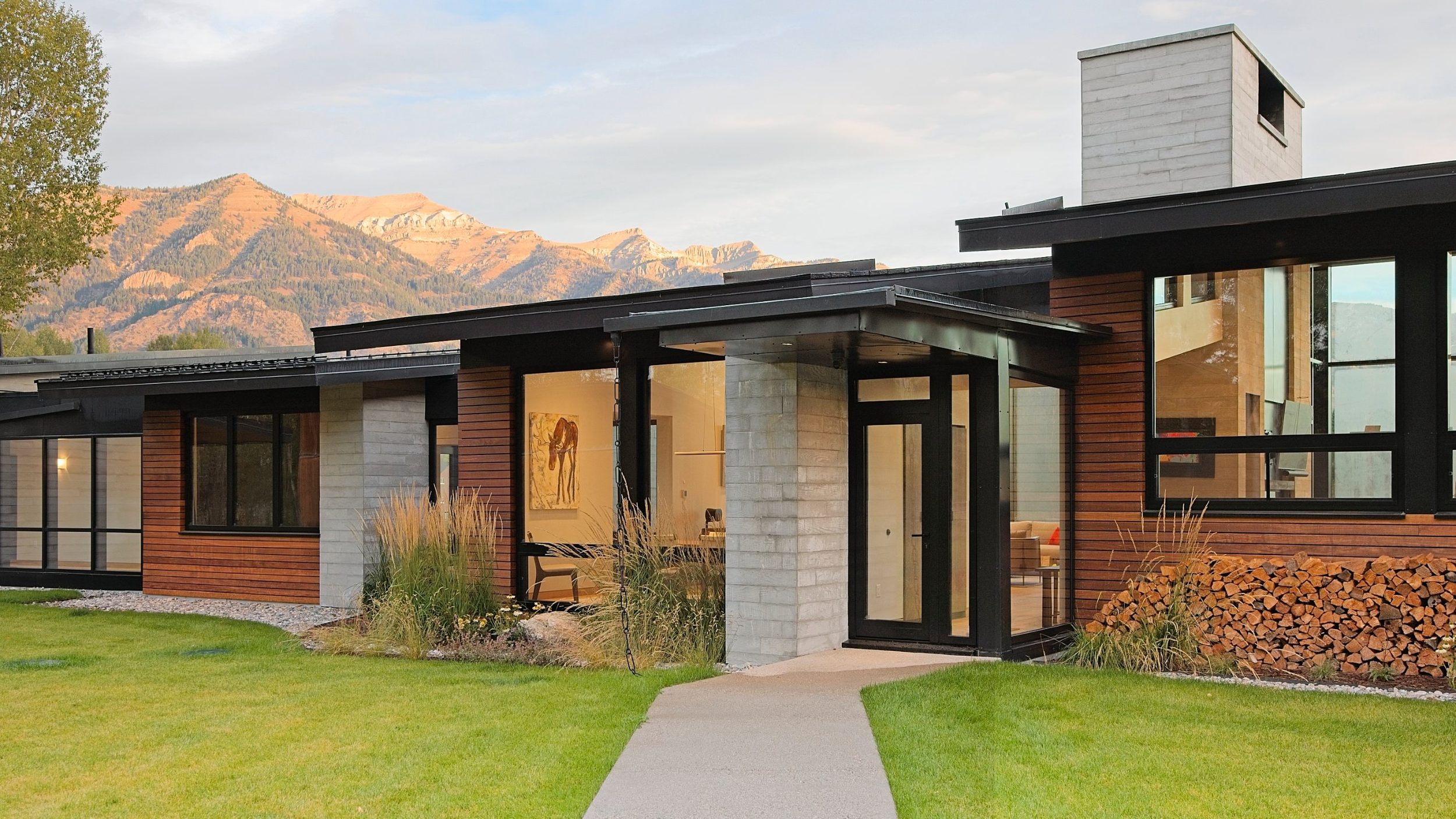 Modern mountain home entry with board-formed concrete piers, hardwood cladding, and flat steel roofs