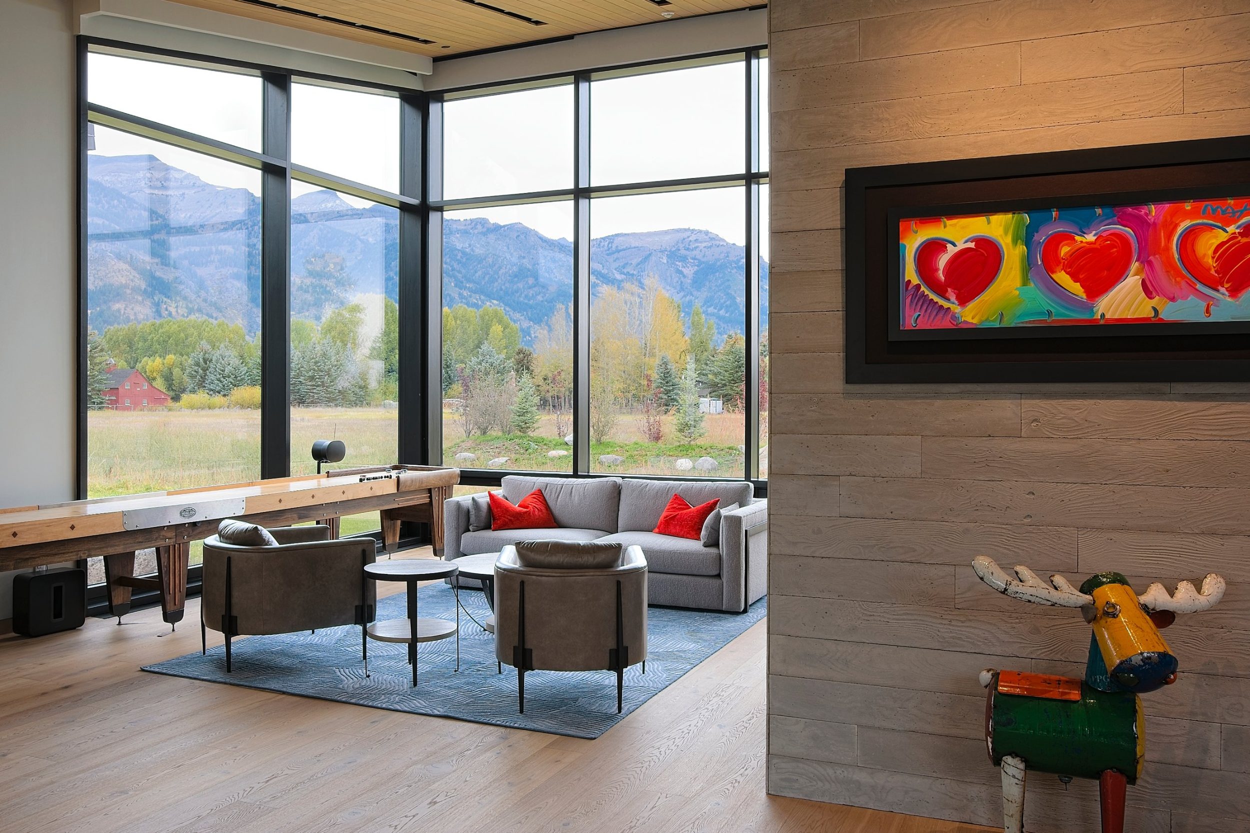 Glass-walled game room with shuffleboard table and seating facing the mountains