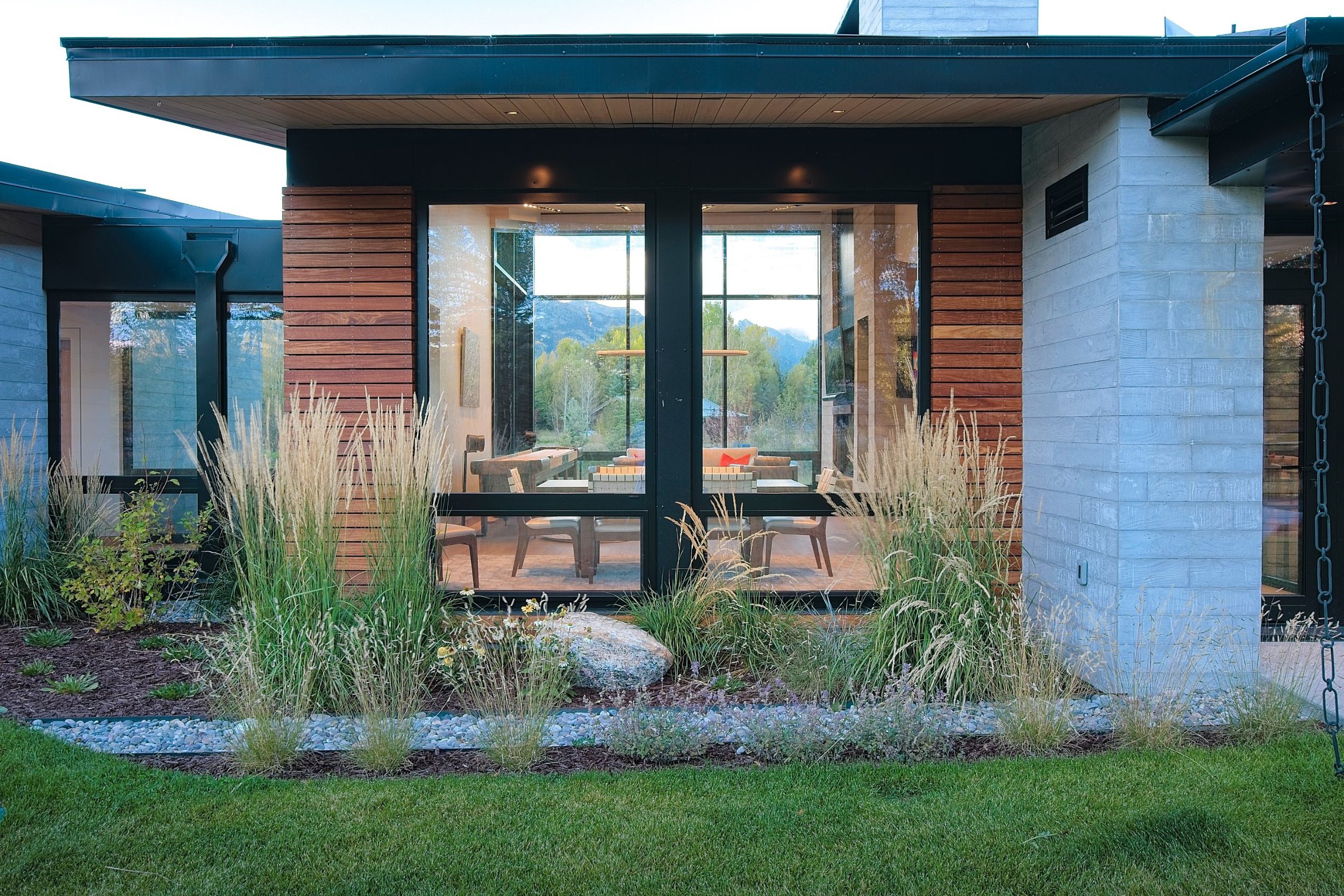 Glass-walled room framed by hardwood cladding and concrete beneath a deep roof overhang, with native grasses